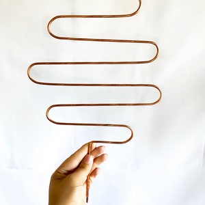 May include: A copper-colored metal hanger with five curved bars. The hanger is designed to hold multiple items, such as scarves, belts, or necklaces.