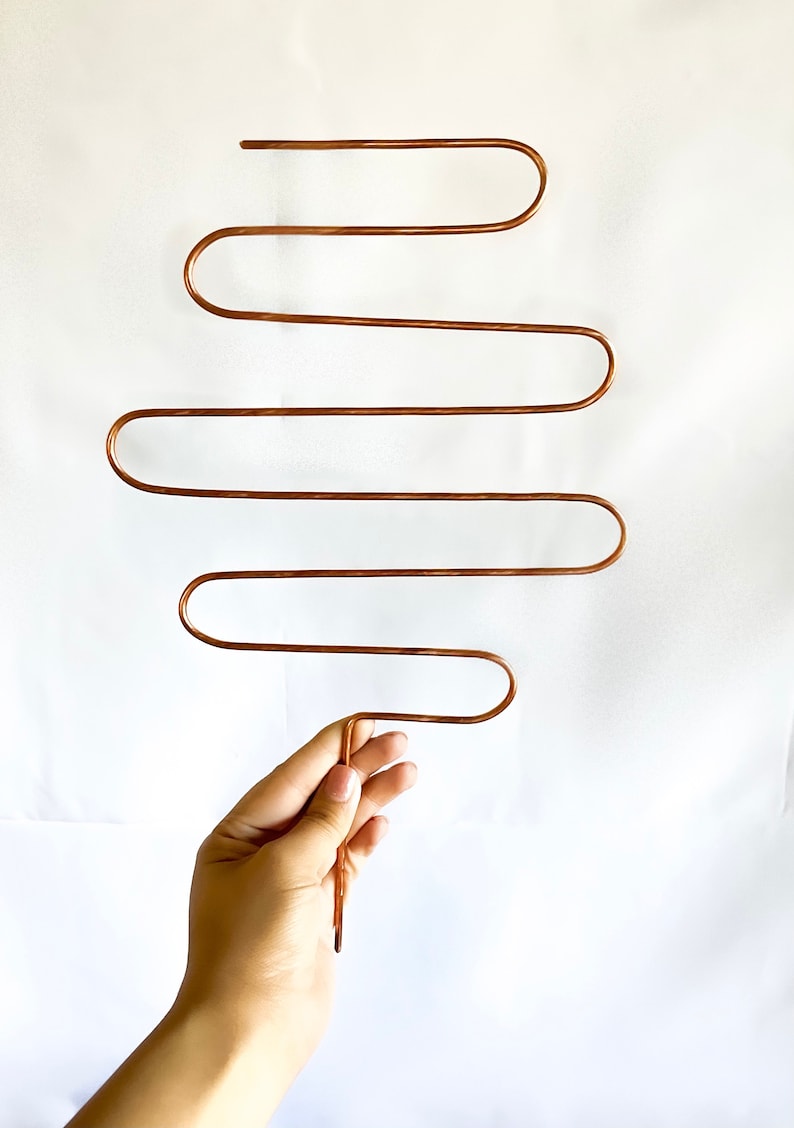 May include: A copper-colored metal hanger with five curved bars. The hanger is designed to hold multiple items, such as scarves, belts, or necklaces.