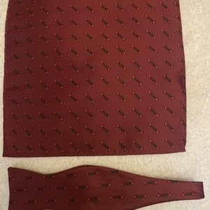 May include: A burgundy bow tie and pocket square with a repeating pattern of the word "KARFO" in black.