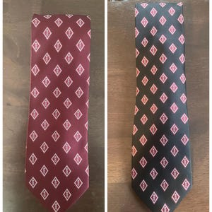 May include: Two neckties, one burgundy and one black, each patterned with repeating white and red diamond shapes. The ties are displayed flat, showcasing their length and design. The burgundy tie is on the left, and the black tie is on the right.