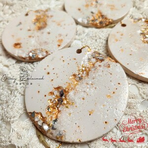 May include: Circular Christmas ornaments with a cream-colored base, adorned with gold and silver accents. The ornaments have a hole at the top for hanging. The text "Chicly Reclaimed Decor" and "Merry Christmas" are visible.