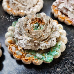 May include: Close-up of a decorative floral design. The design features a textured, off-white flower with gold and green accents. The flower is surrounded by a scalloped edge with speckled details. The text "Chicly Reclaimed Decor" is visible.