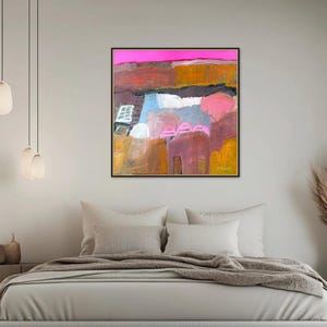May include: Abstract landscape painting in a black frame. The artwork features a vibrant color palette with pink, orange, blue, and yellow hues. The painting is displayed above a bed with neutral-toned bedding.