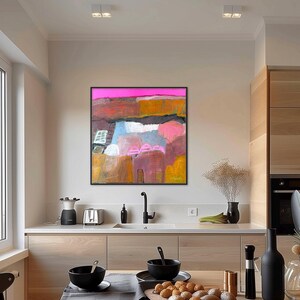 May include: Abstract landscape painting with a black frame. The artwork features a vibrant color palette of pink, orange, blue, and brown hues. The painting is displayed in a modern kitchen setting, adding a touch of artistic flair to the space.