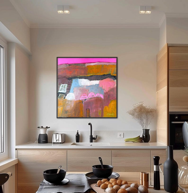 May include: Abstract landscape painting with a black frame. The artwork features a vibrant color palette of pink, orange, blue, and brown hues. The painting is displayed in a modern kitchen setting, adding a touch of artistic flair to the space.