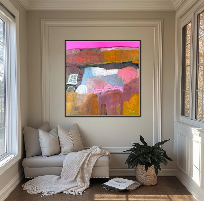 May include: Abstract painting with a black frame. The artwork features a vibrant color palette of pink, orange, blue, and yellow. The painting is displayed above a bench with pillows and a blanket, next to a window and a potted plant.