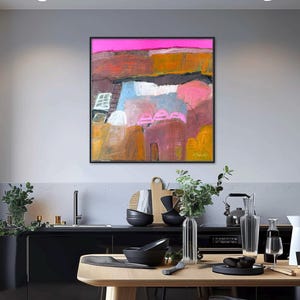 May include: Abstract landscape painting in a black frame. The artwork features a vibrant color palette with pink, orange, blue, and brown hues. The composition includes textured brushstrokes and a dynamic interplay of shapes, evoking a sense of depth and movement.