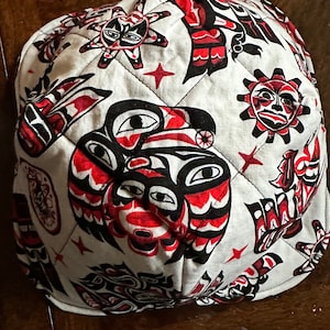May include: A white fabric bowl with a red, black and white pattern of stylised Native American art. The bowl is quilted and has a star design in the centre.