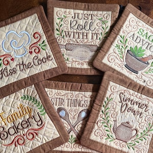 May include: A collection of quilted beige pot holders with brown borders. Each pot holder features embroidered kitchen-themed phrases and images, including "Kiss The Cook," "Just Roll With It," and "Family Bakery."
