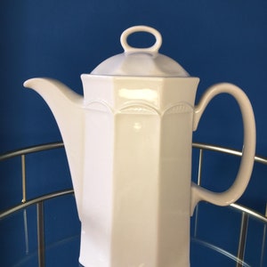May include: White ceramic coffee pot with an octagonal body and a lid with a ring handle. The pot has a spout and a handle.