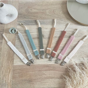 Op de afbeelding: Set van acht stoffen speenkoorden met clips. De speenkoorden zijn in verschillende kleuren, waaronder beige, lichtblauw, roze en bruin. De clips zijn zilverkleurig.