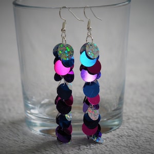 May include: A pair of long silver dangle earrings with iridescent blue, pink, and purple round sequins.