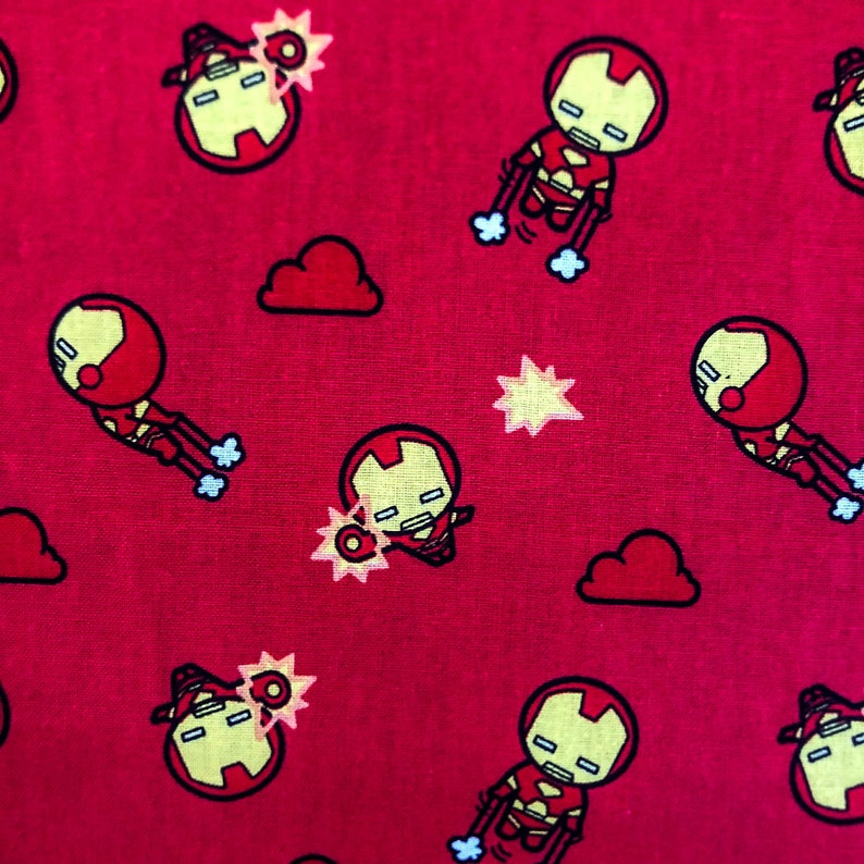 May include: Red fabric with a repeating pattern of a cartoon superhero in a red and yellow suit. The superhero is flying and has a red and yellow starburst behind him. There are also clouds in the pattern.