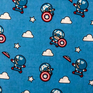 May include: A blue fabric with a repeating pattern of a cartoon superhero wearing a red, white and blue costume. The superhero is holding a red, white and blue shield. The background is a light blue colour with white clouds.