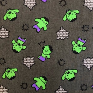 May include: A green fabric with a repeating pattern of a cartoon green character with purple trousers and a black outline. The background is a dark grey with a repeating pattern of a white brick wall.