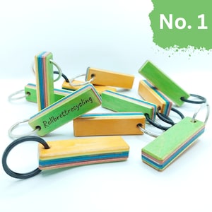 May include: A group of colorful keychains made from recycled skateboard wood. The keychains are in various shades of green, yellow, and brown. One keychain has the text "Rollbrettrecycling" engraved on it.