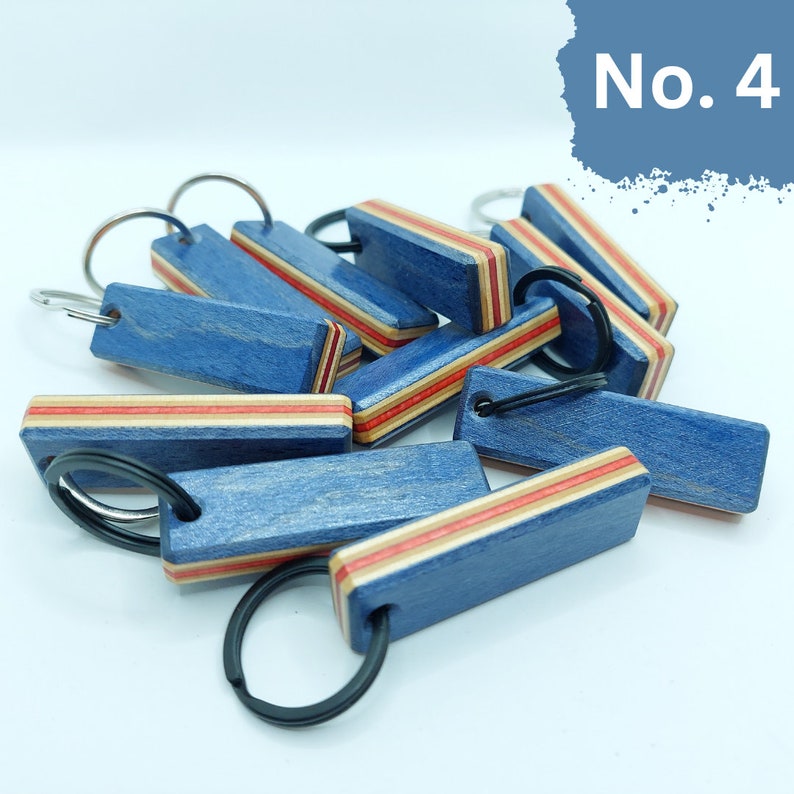 May include: A group of blue and red wooden keychains with a black metal ring. The keychains are made from recycled skateboard wood and have a unique, natural grain pattern.