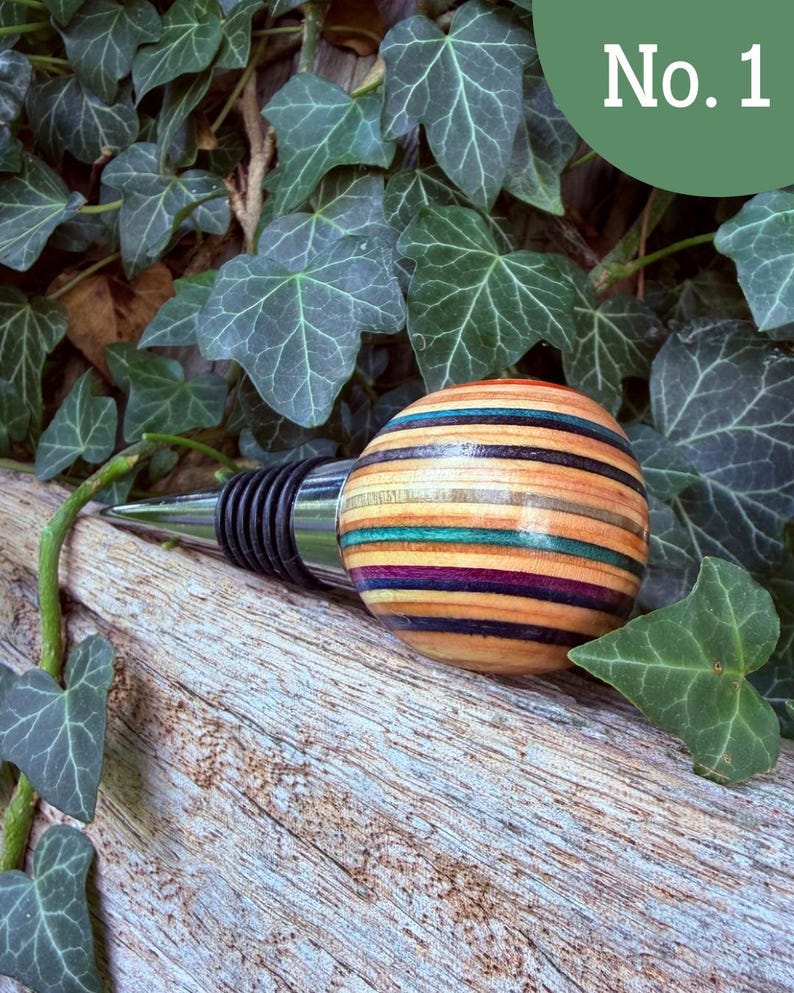 May include: A bottle stopper featuring a spherical handle crafted from multi-colored laminated wood layers in shades of natural tan, teal, purple, and black, attached to a tapered metal base with black rubber rings for a secure seal.
