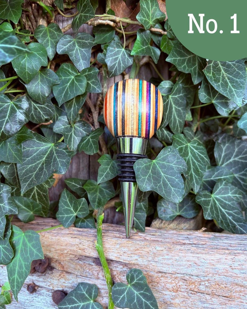 May include: A bottle stopper featuring a spherical top made of multi-colored laminated wood strips in shades of red, orange, yellow, green, blue, and black. The stopper has a silver-toned metal base with black rubber rings for a secure seal.