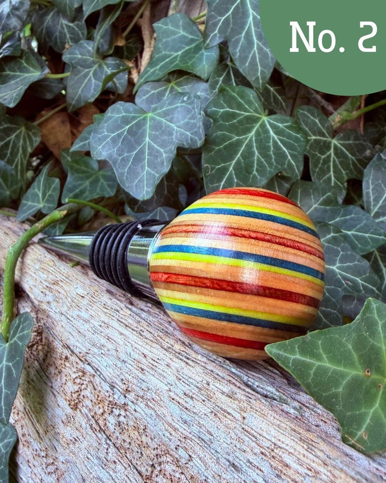May include: A bottle stopper featuring a spherical handle crafted from layers of multi-colored wood in shades of red, yellow, blue, and natural tan. The stopper has a polished chrome metal base with black rubber rings for a secure fit.