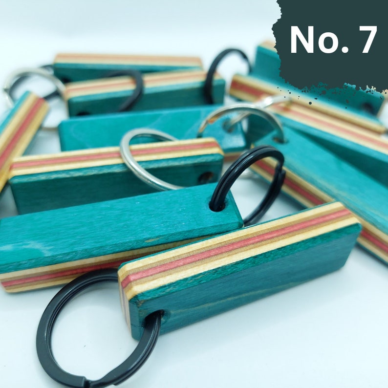 May include: A close-up of a teal and wood keychain with a black key ring. The keychain has a red and white stripe pattern. The keychain is labeled "No. 7".