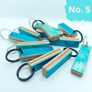May include: A group of teal and red striped wooden keychains with black metal rings. The keychains are made from recycled skateboard decks. The image includes the text "No. 5".