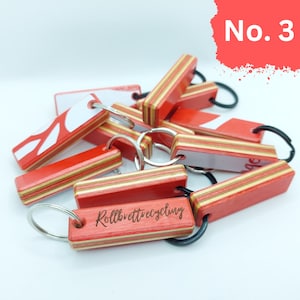 May include: A close-up of a pile of red and white wooden keychains with black metal rings. The keychains are made from recycled skateboards and have the words "Rollbrettrecycling" engraved on one of them.