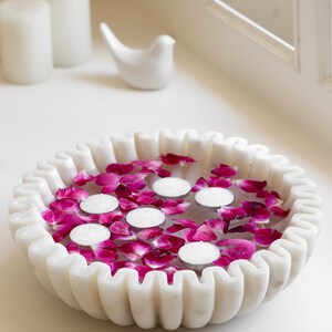 Könnte beinhalten: Weiße Marmor-Schale mit geriffeltem Rand, gefüllt mit Wasser, rosa Rosenblüten und schwimmenden Teelichtern.