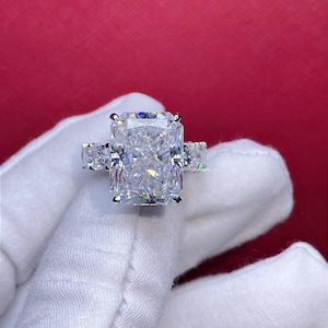 Pode incluir: Um anel de prata com um grande diamante retangular transparente no centro. O diamante &eacute; cercado por diamantes menores na banda.
