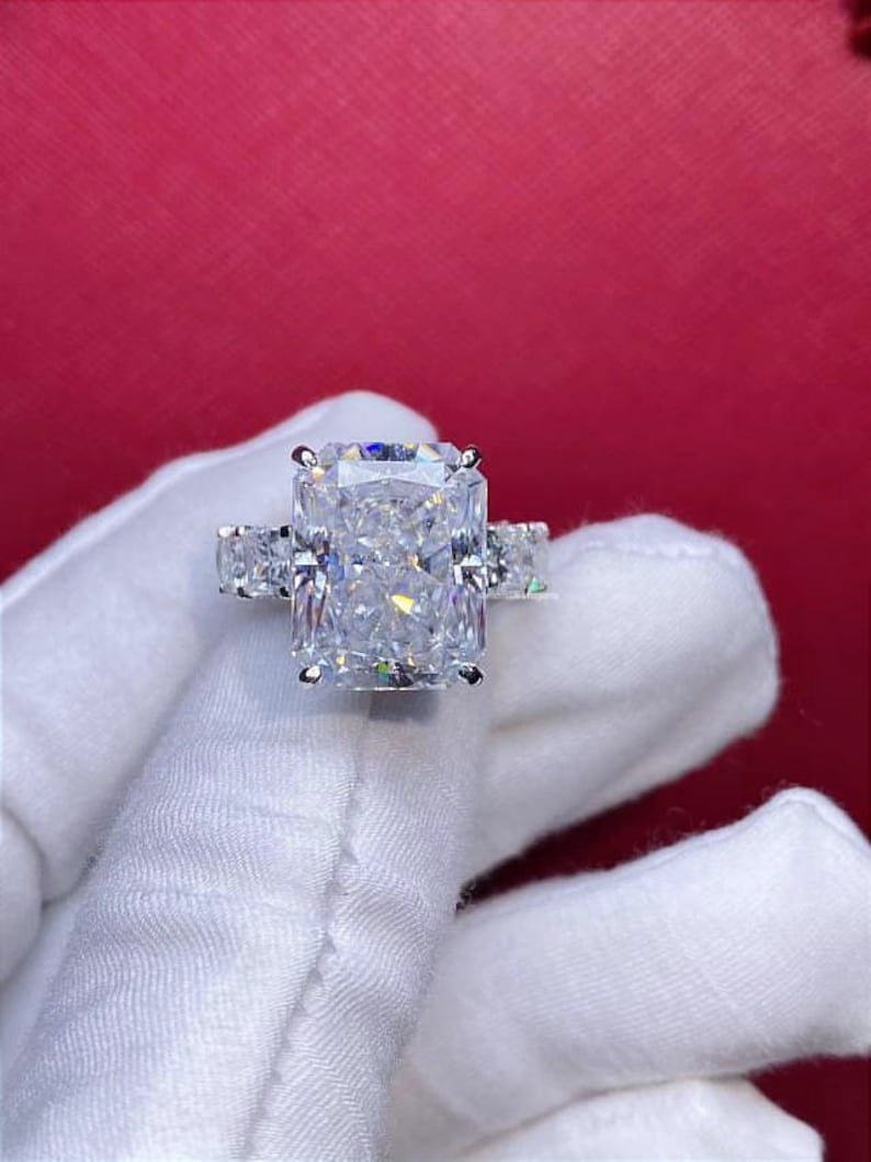 Pode incluir: Um anel de prata com um grande diamante retangular transparente no centro. O diamante &eacute; cercado por diamantes menores na banda.
