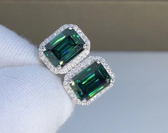 May include: A pair of emerald green gemstone earrings with a halo of smaller white gemstones.