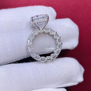Pode incluir: Um anel de prata com um grande diamante quadrado engastado em um halo de diamantes menores. A banda tamb&eacute;m &eacute; engastada com diamantes menores em um design delicado e intrincado.
