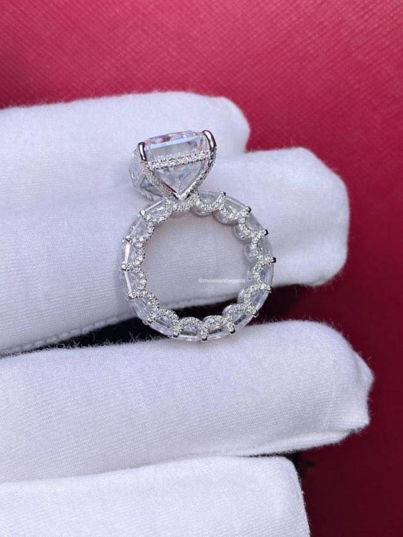 Pode incluir: Um anel de prata com um grande diamante quadrado engastado em um halo de diamantes menores. A banda tamb&eacute;m &eacute; engastada com diamantes menores em um design delicado e intrincado.