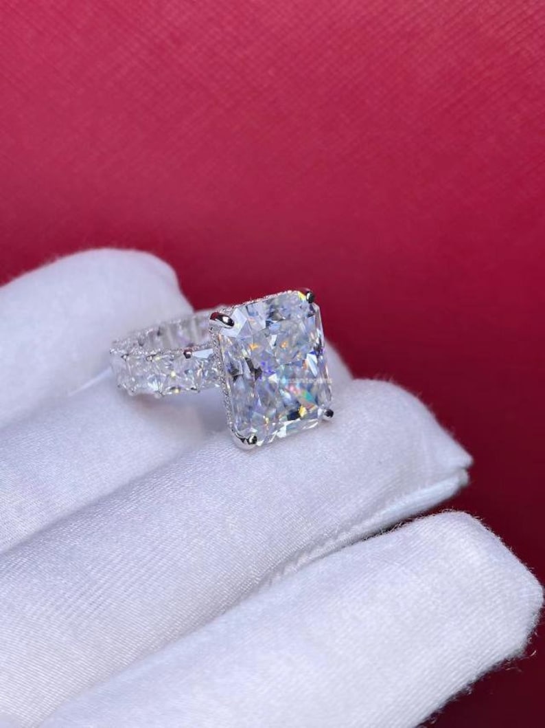 Pode incluir: Um anel de prata com uma grande pedra central de diamante quadrada e transparente. A banda &eacute; adornada com diamantes menores e transparentes.