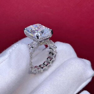 Pode incluir: Um anel de prata com uma grande pedra central de diamante de forma quadrada e uma banda de diamantes menores.