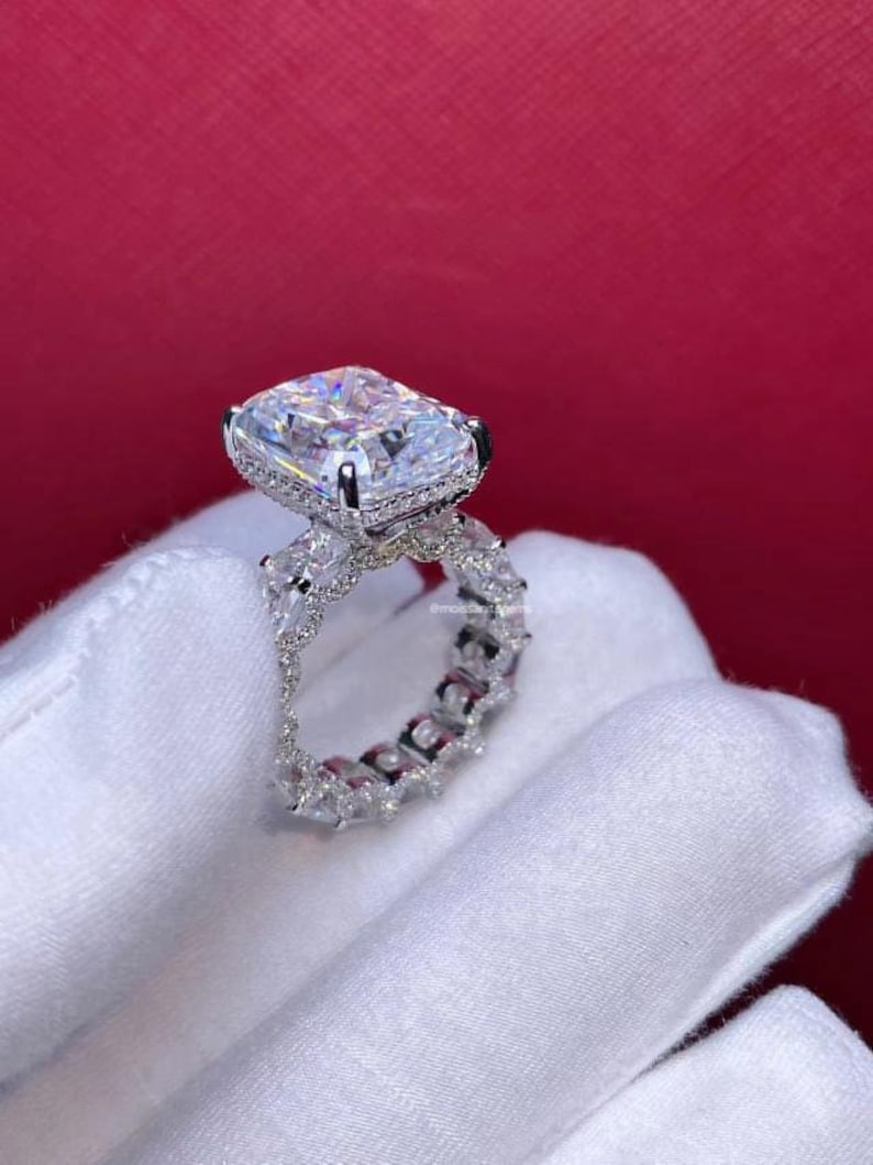 Pode incluir: Um anel de prata com uma grande pedra central de diamante de forma quadrada e uma banda de diamantes menores.