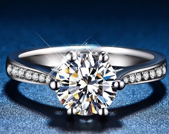 May include: A silver engagement ring with a large, round, clear diamond center stone. The band is accented with smaller diamonds.