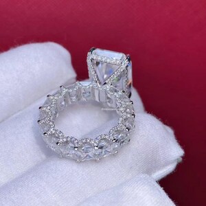 Pode incluir: Um anel de prata com um grande diamante quadrado e uma banda de diamantes menores.