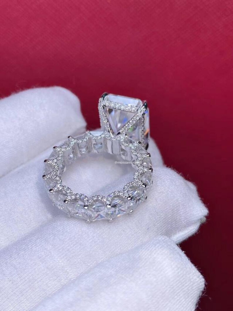 Pode incluir: Um anel de prata com um grande diamante quadrado e uma banda de diamantes menores.