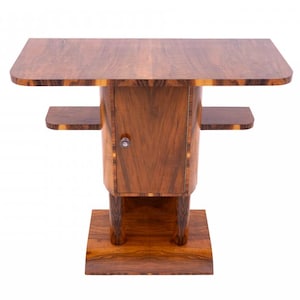 Op de afbeelding: Een houten kast met een rechthoekig bovenoppervlak, een centrale deur met een kleine ronde knop en twee zijplanken. Het meubelstuk rust op een stevige basis en vertoont een opvallend houtnerfpatroon over de gehele bruine structuur.