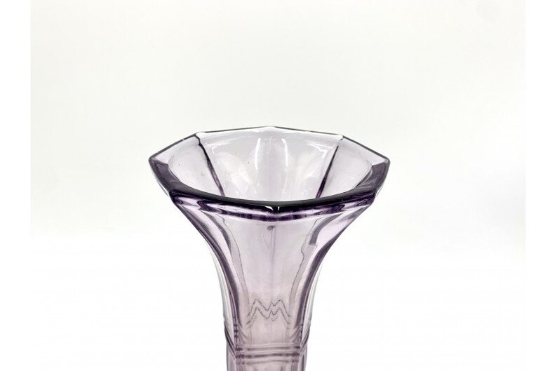 May include: A clear glass vase with a purple tint and a hexagonal opening. The vase has a flared, trumpet-shaped opening and a slender, cylindrical base.