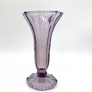 May include: A clear glass vase with a purple tint and a fluted design. The vase has a wide mouth and a narrow base.