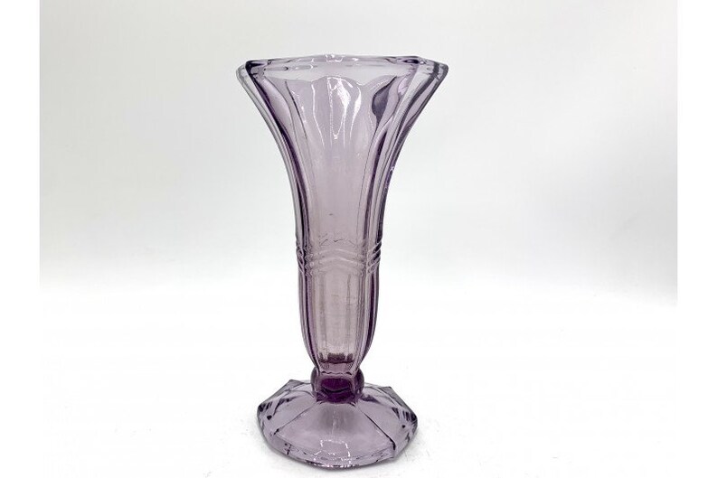 May include: A clear glass vase with a purple tint and a fluted design. The vase has a wide mouth and a narrow base.