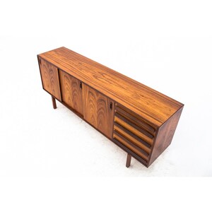 Peut inclure: Un buffet en bois de rose rectangulaire long avec des portes coulissantes et des tiroirs. Le buffet est d'une couleur brun fonc&eacute; riche et a un design moderne et &eacute;l&eacute;gant.
