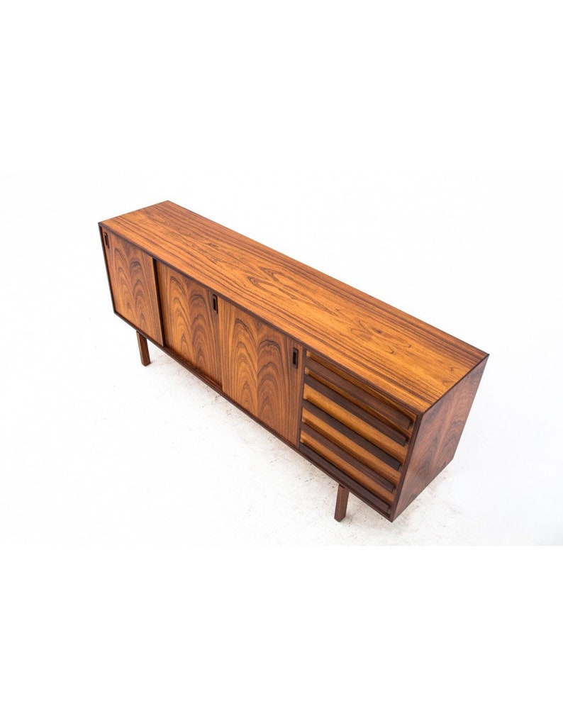 Peut inclure: Un buffet en bois de rose rectangulaire long avec des portes coulissantes et des tiroirs. Le buffet est d'une couleur brun fonc&eacute; riche et a un design moderne et &eacute;l&eacute;gant.