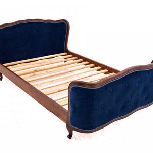 Könnte beinhalten: Ein dunkler Holzbettenrahmen mit einem marineblauen, gepolsterten Kopf- und Fußteil. Das Kopf- und Fußteil hat ein knopfgetuftetes Design. Der Bettrahmen hat Holzlatten.