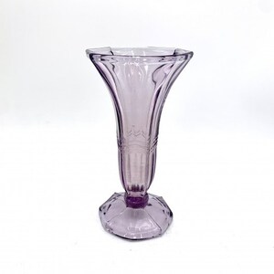May include: A clear, light purple glass vase with a flared top and a faceted base.