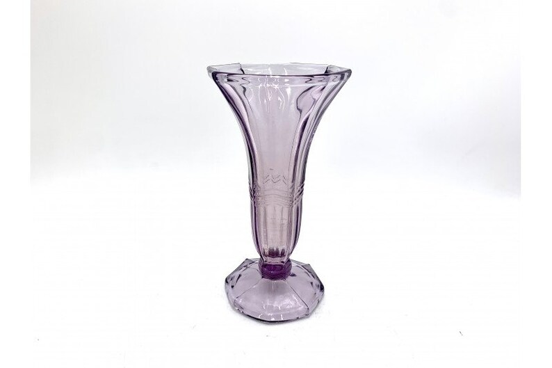 May include: A clear, light purple glass vase with a flared top and a faceted base.