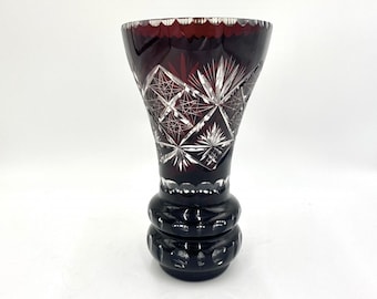 May include: A deep red glass vase with a cut crystal design. The vase has a wide mouth and a narrow base.