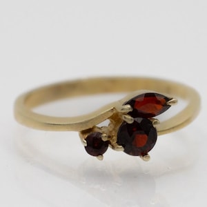 May include: A gold ring with three red gemstones. The ring has a curved band and the gemstones are set in a cluster.